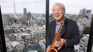 Ein Mann posiert mit Altsaxofon vor einem Fenster. Im Hintergrund ist die Stadt Tokio zu sehen. © Toshiyuki Kon / picture alliance Foto: Toshiyuki Kon