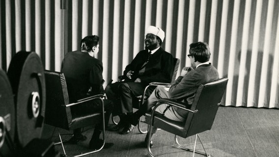 Zwei Männer interviewen mit einem Mann mit Hut. © https://creativecommons.org/licenses/by/2.0/deed.en Foto: Unbekannt