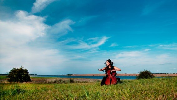 Frau mit Cello sitzt in einer Wiese © Felix Broede Foto: Felix Broede