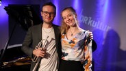 Ein junger Mann mit einer Trompete in der Hand steht neben einer jungen Frau, die beide in die Kamera lächeln. © Franziska Dieckmann / NDR Foto: Franziska Dieckmann / NDR