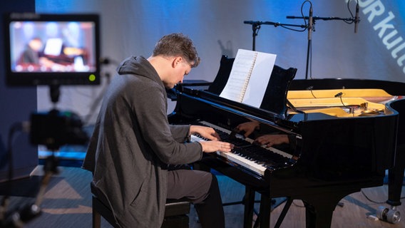 Ein Mann, der dunkel gekleidet ist, sitzt vor einem schwarzen Flügel. Seine Hände liegen auf den Tasten und er ist vertieft in die Musik. © Ekaterina Shurygina / NDR Foto: Ekaterina Shurygina / NDR