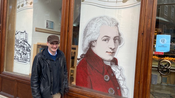 Ein Mann steht lachend vor einer Abbildung Mozarts in einem Schaufenster. © NDR Foto: Friederike Westerhaus