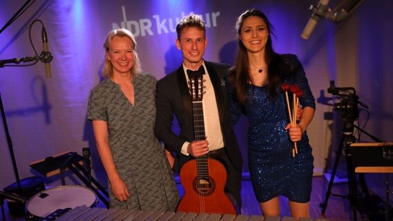 In der Mitte steht ein junger Mann mit einer Gitarre in der Hand und rechts und links neben ihm eine Frau. © Claudius Hintzmann / NDR Foto: Claudius Hintzmann / NDR