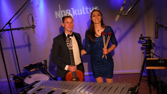 Links steht ein junger Mann mit einer Gitarre in der Hand und neben ihm eine junge Frau mit einem blauen Glitzerkleid. © Claudius Hintzmann / NDR Foto: Claudius Hintzmann / NDR