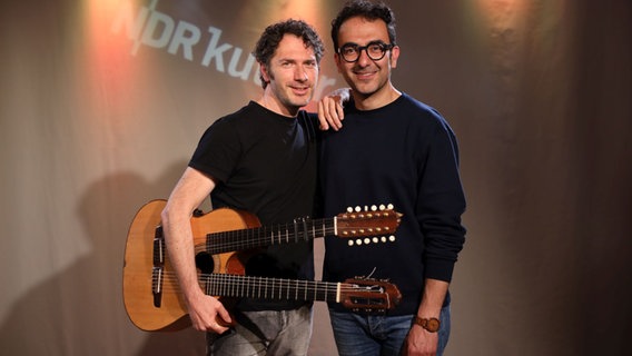Zwei Männer stehen nebeneinander. Einer hält eine Gitarre mit zwei Hälsen in der Hand. © Franziska Dieckmann / NDR Foto: Franziska Dieckmann / NDR