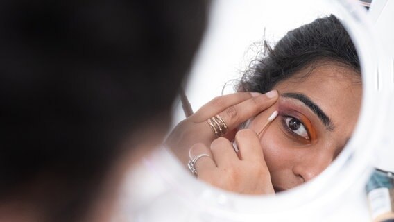 Eine Frau schminkt ihre Augen und blickt dabei in den Spiegel. © NDR Foto: Benjamin Hüllenkremer
