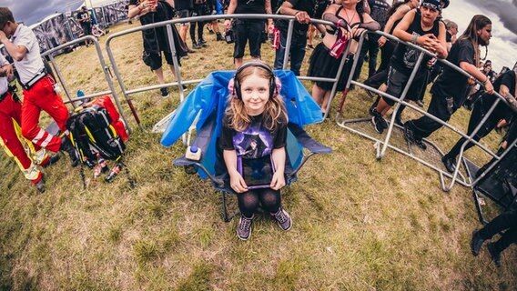 Ein Kind mit Ohrschützern sitzt im Fotografengraben vom Gothic-Musikfestival M'era Luna 2023 © NDR Foto: Benjamin Hüllenkremer