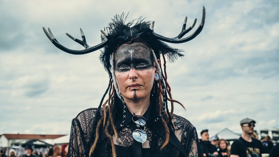Eine Besucherin mit geschminktem Gesicht und einem Geweih auf dem Kopf beim Gothic-Musikfestival M'era Luna 2023. © NDR Foto: Benjamin Hüllenkremer