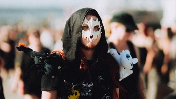 Ein Mann mit einer weißen Maske, Kapuze und schwarzer Kleidung läuft auf dem Festival M'era Luna 2023 herum © M'era Luna 2023 /  Christoph Eisenmenger Foto: Christoph Eisenmenger
