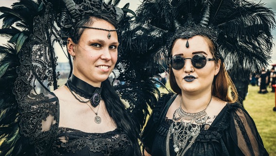 Zwei Frauen mit schwarzen Hörnern und aufwendigem Kopfschmuck aus schwarzen Federn beim Festival M'era Luna 2023 © NDR Foto: Benjamin Hüllenkremer