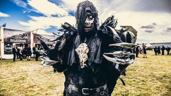 Ein Fan mit aufweniger Maske und Kostüm in Schwarz mit Metallkrallen, einem Tierschädel um den Hals  bei M'era Luna 2023 © NDR Foto: Benjamin Hüllenkremer