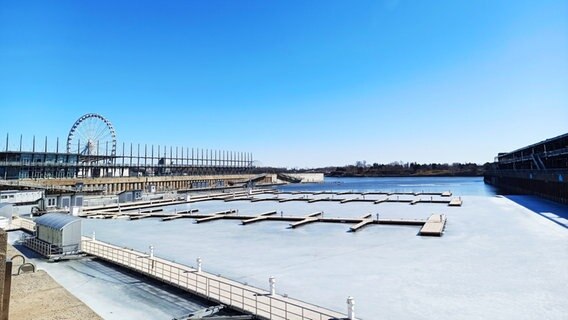 Abgebildet ist der alte Hafen von Montréal, es liegen keine Schiffe im Hafen und auf dem Wasser ist eine Eisschicht, der Himmel ist blau und auf der linken Seite steht ein Riesenrad. © Eva Schramm / NDR Foto: Eva Schramm