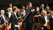 Die Münchner Philharmoniker und Dirigent Lahav Shani stehen auf der Bühne. © Tobais Hase 