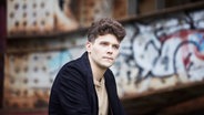 Pianist Szymon Nehring sitzt vor einer Graffitiwand © Bartek Barczyk 