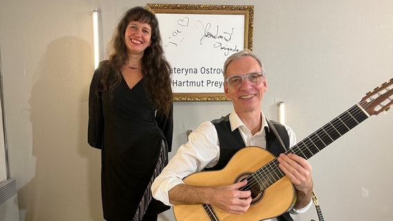 Eine Frau steht neben einem Mann, der sitzt und hält eine Gitarre. Beide lächeln freundlich in die Kamera. © Claus Röck / NDR Foto: Claus Röck