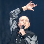 Der Sänger Peter Gabriel in schwarz-grauem Oberteil mit Stehkragen singt mit dem Mikro in der linken, die rechte Hand über dem Kopf erhoben © Hannes P. Albert/dpa +++ dpa-Bildfunk +++ Foto: Hannes P. Albert
