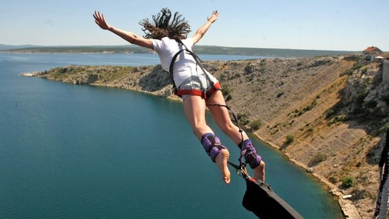 Eine Frau mit ausgebreiteten Armen springt mit Bungee-Seil über der kroatischen Küste von der Brücke Maslenika © picture alliance / PIXSELL | Dino Stanin/PIXSELL Foto: Dino Stanin