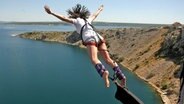 Eine Frau mit ausgebreiteten Armen springt mit Bungee-Seil über der kroatischen Küste von der Brücke Maslenika © picture alliance / PIXSELL | Dino Stanin/PIXSELL Foto: Dino Stanin