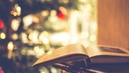 Ein aufgeschlagenes Buch liegt vor einem Weihnachtsbaum. © Christine ten Winkel / photocase.de 