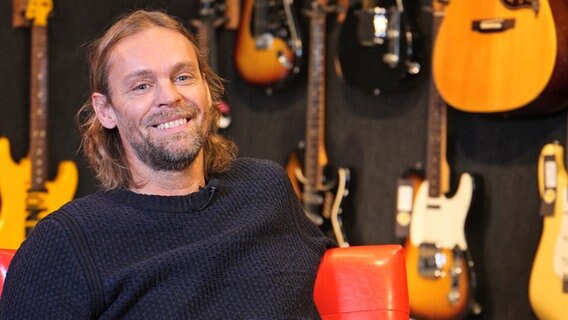 Der Hamburger Musiker Ingo Pohlmann lächelt in Umgebung von Gitarren © NDR Foto: Aaron Moser
