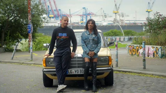 Denyo und Rapperin Eunique lehnen an einem Auto am Hamburger Hafen © Screenshot NDR 