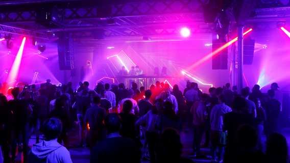 Tanzende Menschen in einer Discothek, drumherum rote Scheinwerfer © picture allliance 