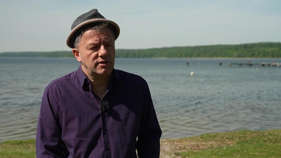 Ein Mann mit Hut steht vor einem See © NDR 
