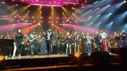 Sängerinnen und Sänger stehen auf einer pinkfarben angestrahlten Bühne und singen © NDR / Uli Kniep Foto: Uli Kniep
