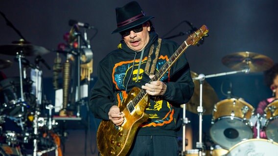 Der Musiker Santana mit goldener Gitarre und schwarzem Hut auf der Bühne © picture alliance/dpa/Invision/AP Foto:  Amy Harris