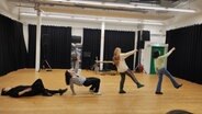 In einem Theaterprobenraum liegt eine Frau auf dem Boden (links), eine Frau stützt sich zum Aufstehen hoch, zwei weitere Frauen gehen. In einem Theaterprobenraum liegt eine Frau auf dem Boden (links), eine Frau stützt sich zum Aufstehen hoch, zwei weitere Frauen gehen. © NDR / Svenja Estner Foto: Svenja Estner