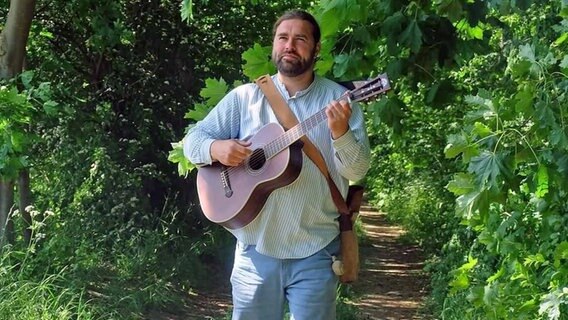 Der Musiker Sebastian Sack geht Gitarre spielend einen Waldweg entlang. © Sabastian Sack 