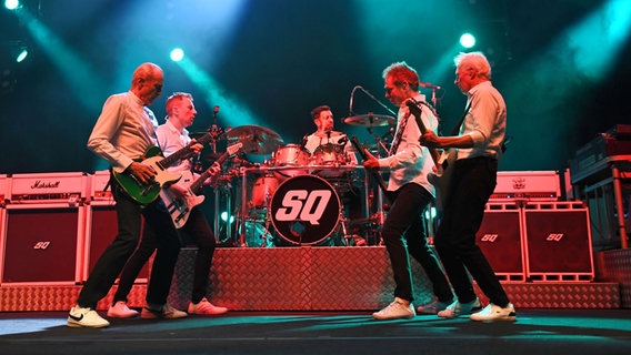 Vier Männer stehen auf einer Bühne mit Gitarren und einem Bass. Im Hintergrund sitzt der Schlagzeuger. © picture alliance / Captital Pictures | Martin Harris Foto: Martin Harris