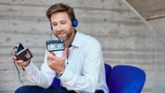 Mann sitzt auf einem Stuhl und hört Musik vom Walkman. © photocase.de Foto: Westend61