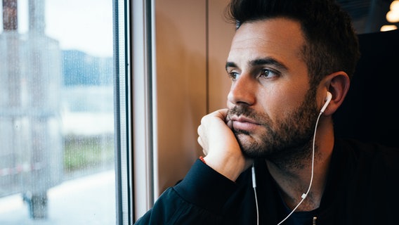 Mann mit Kopfhörern schaut im Zug aus dem Fenster. © photocase.de Foto: Marjan Apostolovic