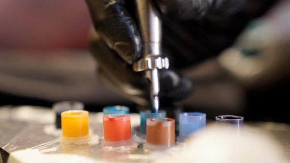 Tattoo-Farben stehen auf einem Tisch in einem Tätowierstudio. © picture alliance/dpa | Marcus Brandt 