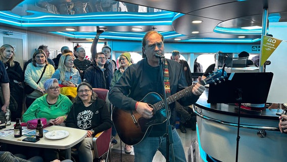 Thees Uhlmann singt und spielt Gitarre in einer Gruppe von Menschen auf einem Schiff. © NDR.de/Laura Albus 