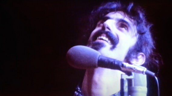 Frank Zappa bei einem Konzert blickt lächelnd nach oben. © picture alliance / Everett Collection | ©Magnolia Pictures/Courtesy Everett Collection 