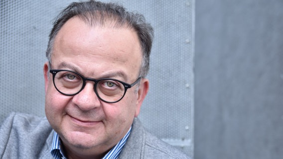 Albert Wiederspiel, Leiter des Filmfests Hamburg lächelt in die Kamera. Er trägt ein graues Sacko und darunter ein blau, weiß karriertes Hemd. © Hamburg Filmfest Foto: Heike Blenk