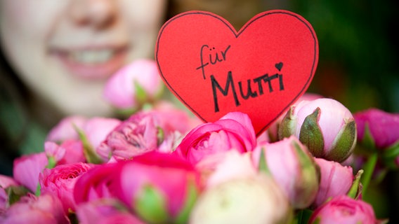 Eine junge Frau mit einem Blumenstrauß, auf dem "Für Mutti" steht. © picture alliance / dpa Themendienst Foto: Mascha Brichta