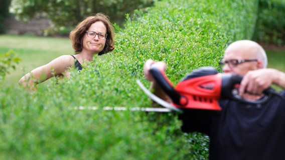 Eine Frau schaut skeptisch auf ihren Nachbarn, der die Gartenhecke stutzt. © picture alliance / photothek | Thomas Trutschel 