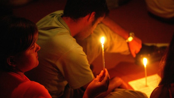 Eine Frau und ein Mann sitzen mit zwei Kerzen im Dunkeln. © picture-alliance / Godong Foto: Pascal Deloche