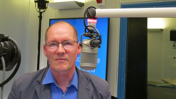 Ein Mann mit Brille, blauem Hemd und Sakko sitzt an einem Mikrofon und blickt in die Kamera © NDR Foto: Axel Seitz