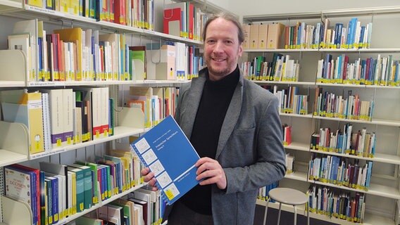 Christoph Schmidt steht vor einem Bücherregal und hält ein Friesischlernbuch in der Hand © NDR.de/ Peer-Axel Kroeske Foto: Peer-Axel Kroeske