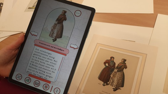 Eine Zeichnung einer Frau in Tracht auf dem Handybildschirm und auf einem Blatt Papier. © NDR Foto: Lina Bande
