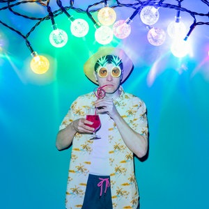 Ein Mann, der einen Cocktail trinkt steht unter einer Party-Lichterkette. © Sinje Hasheider Foto: Sinje Hasheider