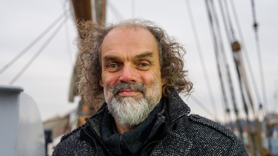 Der Frontman der Band Santiano Hans-Timm Hinnrichsen steht auf einem Segelschiff und lächelt in die Kamera. © NDR 