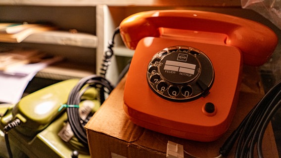 Ein nostalgisches orangefarbenes Telefon mit Wählscheibe. © NDR Foto: Lornz Lorenzen