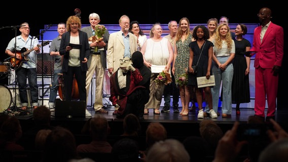 Die Gewinner und Gewinnerinnen des plattdeutschen Schreibwettbewerbs "Vertell doch mal" stehen gemeinsam auf der Bühne. © NDR Foto: Lornz Lorenzen