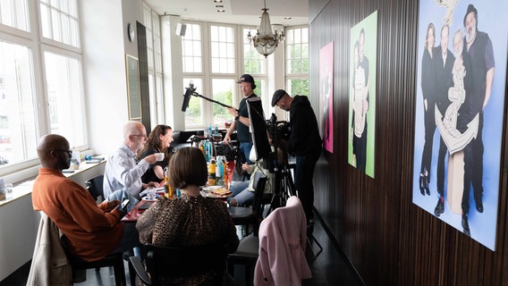 Die Mitglieder der Ehrenjury von "Vertell doch mal" sitzen gemeinsam an einem Konferenztisch und werden gefilmt. © NDR Foto: Lornz Lorenzen