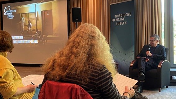 Der künstlerische Leiter der Nordischen Filmtage Thomas Hailer erläutert welche Filme zu sehen sind. Dabei schaut er nach rechts zu einer Leinwand, auf der Filme gezeigt werden.  Foto: Linda Ebener